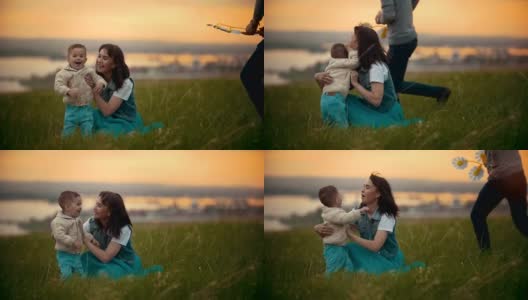 年轻的妈妈和她的孩子在草地上玩耍，孩子是快乐的，夏天的傍晚，夕阳高清在线视频素材下载