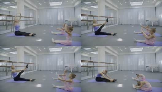 首席芭蕾舞演员教两个孩子如何在宽敞明亮的体育馆里伸展腿高清在线视频素材下载