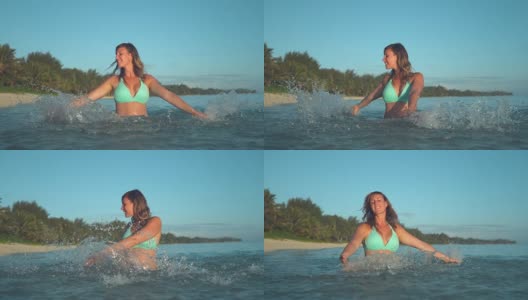 慢镜头:身着绿松石色衣服的快乐女子在透明的水中拖动手指。高清在线视频素材下载