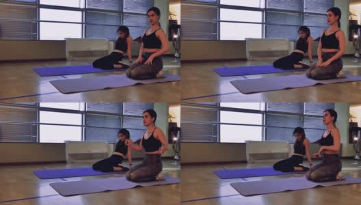 在健身房里，两名女运动员做完练习后坐在瑜伽垫上休息。高清在线视频素材下载