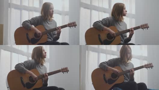 在一间白色的房间里，一个金发女孩在美丽的阳光下用原声吉他享受着美妙的旋律。高清在线视频素材下载