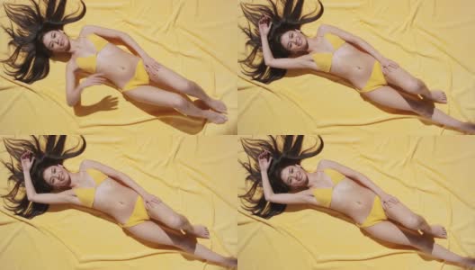 穿着泳衣的女人躺在黄色的沙滩毯上晒太阳高清在线视频素材下载