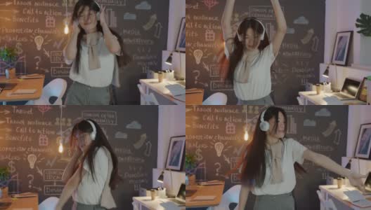 美丽的亚洲女孩员工在工作场所跳舞戴耳机享受音乐在晚上高清在线视频素材下载
