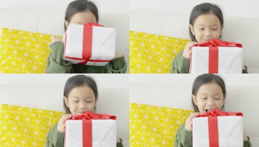 亚洲女孩在家里的沙发上拿着带红丝带的礼盒，假日概念。高清在线视频素材下载