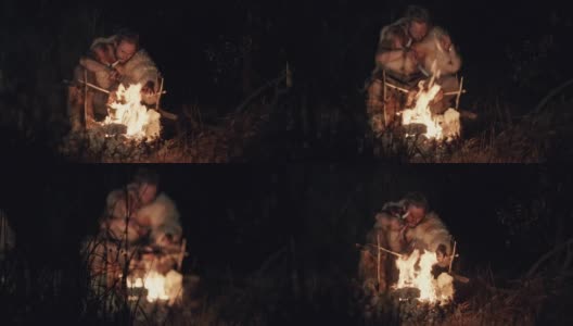 一个披着兽皮的大胡子男人，晚上在乡下，在火边休息，吃苹果。晚上在火边吃东西的野蛮人高清在线视频素材下载