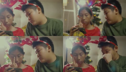 快乐的亚洲儿童穿着毛衣和发带使用智能手机和平板电脑在晚上一起在家里以圣诞装饰为背景，假日概念。高清在线视频素材下载