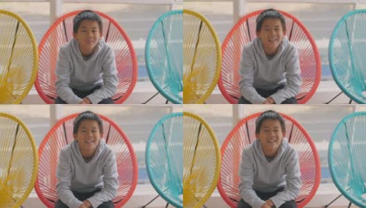 快乐和自信的混血儿亚洲男孩微笑和坐在彩色的红色椅子，青少年肖像高清在线视频素材下载