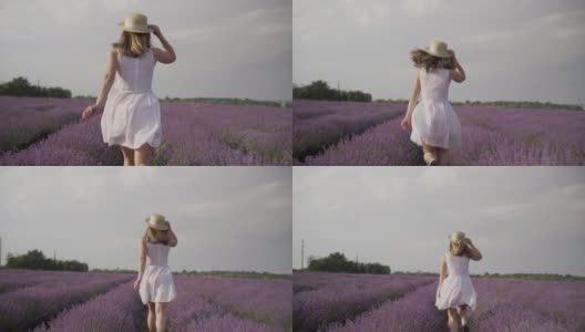 女孩在夏日夕阳下的薰衣草地里奔跑。普罗旺斯的花丛薰衣草和一个年轻女人。一位穿着裙子，戴着帽子的女士。芳香疗法和放松的概念高清在线视频素材下载