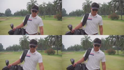 一名亚洲男子高尔夫球手步行和携带高尔夫球袋在高尔夫俱乐部高清在线视频素材下载