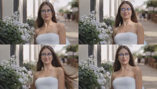 迷人的年轻女子，长发，戴眼镜站在鲜花附近的街道高清在线视频素材下载