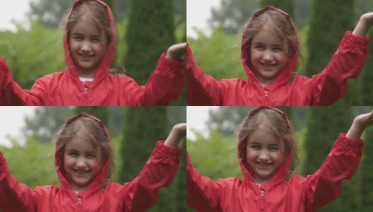 快乐的小女孩在雨中微笑。孩子热爱自然，幸福自由。孩子玩雨滴雨。孩子在下雨的夏天在户外玩耍。穿红雨衣的女孩欣赏秋日降雨。高清在线视频素材下载