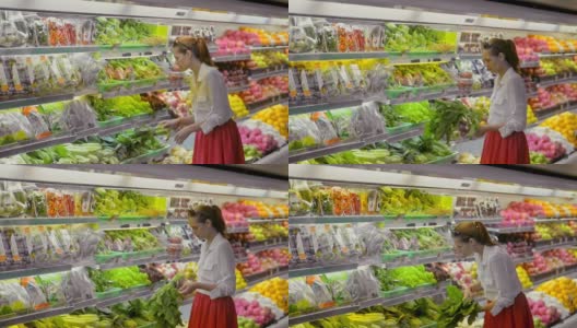 超市里的新鲜蔬菜。女人在挑选冰箱里的生菜高清在线视频素材下载