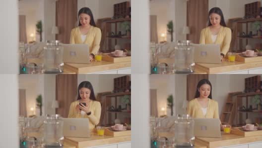 亚洲中国美女检查她的电话信息在厨房柜台在她的笔记本电脑在周末高清在线视频素材下载