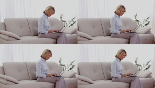 一个成熟的女人坐在沙发上用着笔记本电脑高清在线视频素材下载