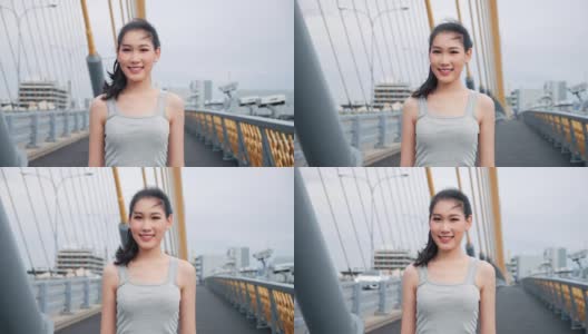 美丽的亚洲女人看着镜头微笑迷人优雅的亚洲女士在高速公路大桥街道城市的运动胸罩肖像。4 k慢动作。高清在线视频素材下载