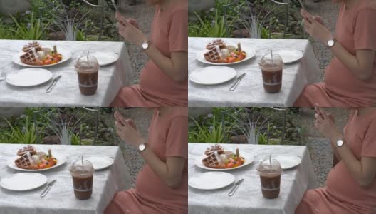一位怀孕的亚洲妇女坐在咖啡店里摸着自己的肚子高清在线视频素材下载