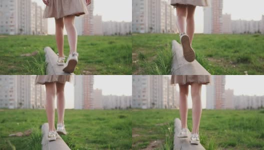 小女孩的双腿在城市草坪上的混凝土圆木上行走高清在线视频素材下载