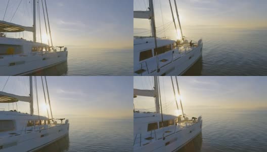 航拍侧视图拍摄的三个美丽的健康妇女做早晨瑜伽在一艘白色帆船双体船。平静的大海与升起的太阳和平静的大海。高清在线视频素材下载