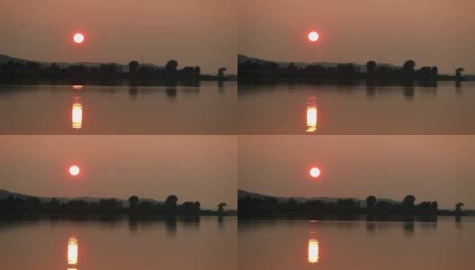 河上的日落。一个明亮的火红的黄色球坐在森林后面。前景是一条宽阔的河流高清在线视频素材下载