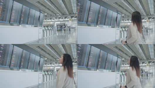 一名亚洲女性旅客在机场，看着她旅行的航班带着行李，在屏幕上看到航班号就开始了新的旅行，旅行度假高清在线视频素材下载