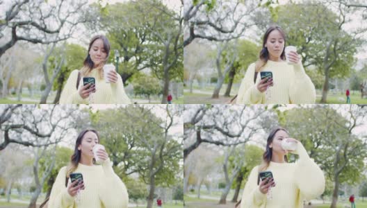 一段4k视频记录了一位迷人的年轻女子边喝咖啡边发短信边走过公园高清在线视频素材下载