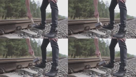 一个戴着头盔的铁路工人正在修理铁路，用大锤敲打着铁路的塔尖。高清在线视频素材下载