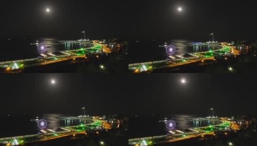 一个大城市的夜景，摩天轮的背景海和月球的路径。路上的交通。时间流逝高清在线视频素材下载