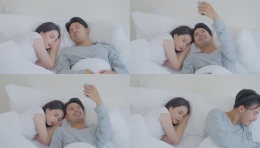 亚洲魅力有趣的男性自拍与睡觉的女友在床上。幸福的家庭，新婚夫妇一起度过早上的时间，丈夫躺在卧室里给妻子拍照。高清在线视频素材下载
