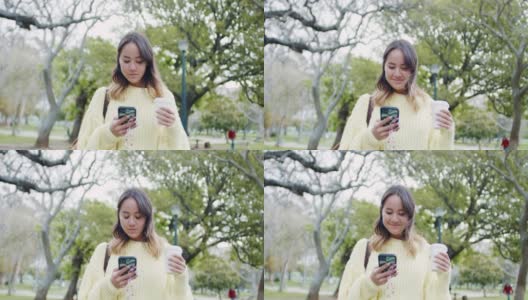 一段4k视频记录了一位迷人的年轻女子边喝咖啡边发短信边走过公园高清在线视频素材下载
