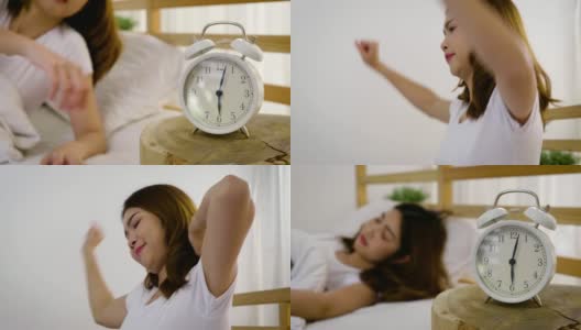 年轻美丽的亚洲女人醒来和伸展在她的床在家里，闹钟醒来的概念高清在线视频素材下载