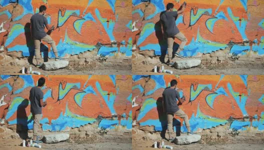 涂鸦艺术家在华尔街墙上作画。帅哥用喷雾器喷瓶喷彩色涂料，都市户外艺术概念。缓慢的运动。后视图，总体规划高清在线视频素材下载