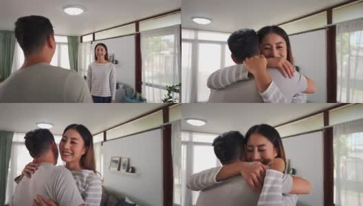 一个30多岁的年轻亚洲男人在家里的客厅里跑着去拥抱一个微笑的女人。幸福的丈夫和妻子拥抱和度过家庭时间一起在舒适的房子。团聚和关系的生活理念高清在线视频素材下载