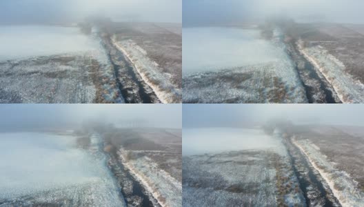 在一个霜冻和雾蒙蒙的早晨，一场雪之后，一条小河从荒地流向树木的无人机视图高清在线视频素材下载