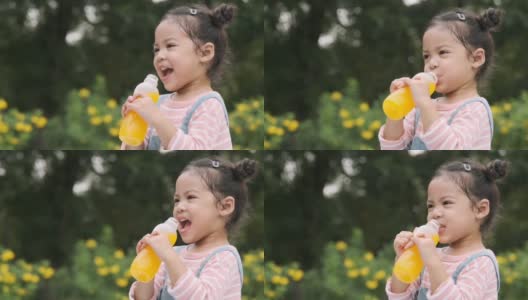 可爱的小女孩拿着一瓶橙汁在花园里喝，慢镜头拍摄。高清在线视频素材下载