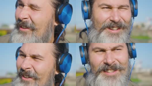 留着胡子的中年男子戴着耳机听着音乐，跟着音乐唱歌，并随着音乐的节拍点头。面部特写高清在线视频素材下载