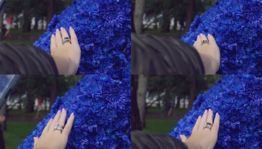 一个女孩用智能手机拍下了她的手，在亮蓝色花朵的背景下，她修剪着漂亮的指甲。带着智能手机和社交网络在公园里散步高清在线视频素材下载