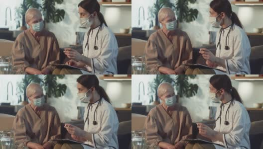 家访时，身穿白大褂的年轻女医生向戴口罩的老年妇女展示装有疫苗的药瓶。高清在线视频素材下载