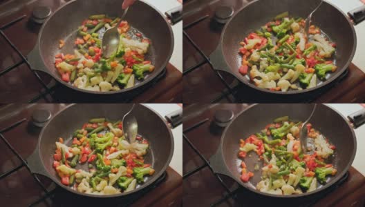 白种人的手搅拌蔬菜在煎锅与不锈钢勺子，而煎，特写高清在线视频素材下载