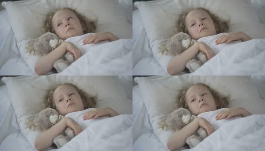 伤心的小女孩带着玩具在床上哭泣，不开心的生病的孩子感到孤独高清在线视频素材下载