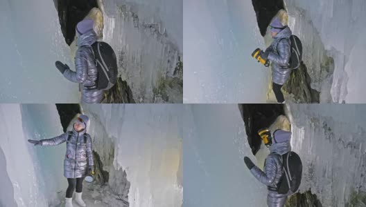 贝加尔湖冰洞上的女游客。冬岛之旅。女孩背包客正在冰洞中行走。游客看着美丽的冰洞。徒步旅行者穿银色夹克，背包，led灯。高清在线视频素材下载