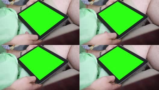 一个白人男性在客厅扶手椅上看一个普通的绿色屏幕平板电脑高清在线视频素材下载