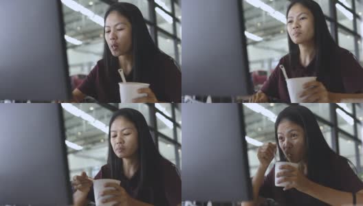 亚洲自由职业者妇女吃方便面杯和工作在电脑屏幕前高清在线视频素材下载