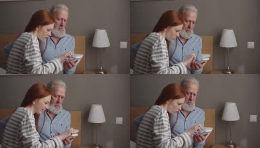 快乐的红发孙女用手机给坐在家里床上的白发爷爷拍照。高清在线视频素材下载