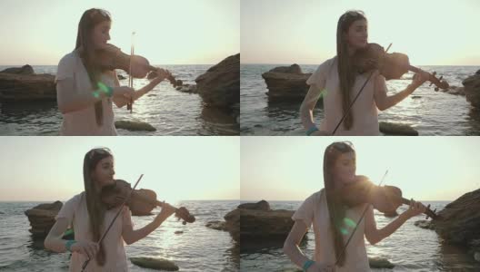 年轻美丽的白人女孩穿着牛仔裤在海滩上拉小提琴靠近美丽的大海或海洋，慢镜头高清在线视频素材下载