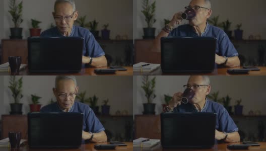 年长的自由职业男性作家戴着眼镜，在晚上用笔记本电脑打字，喝着热咖啡。资深作家在家里的桌子上用电脑工作。居家办公高清在线视频素材下载