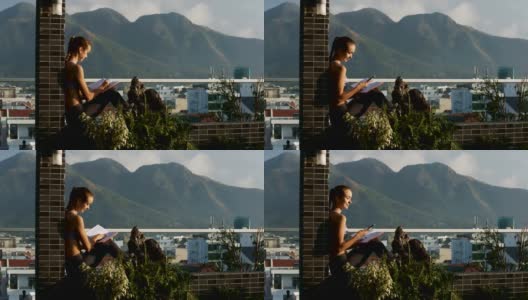 坐在阳台墙上的盆栽上的女孩正在拿手机高清在线视频素材下载