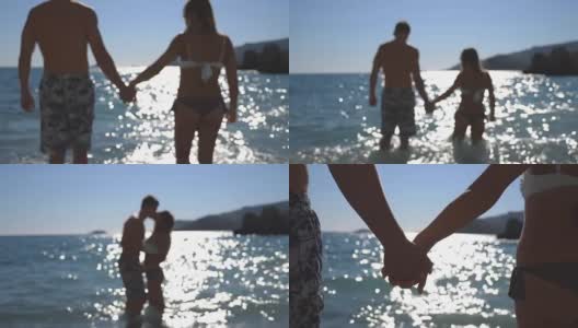 在阳光明媚的日子里，年轻的一对手牵着手走向大海。美丽的夫妇亲吻靠近海岸与阳光反射在水面上的背景。爱和幸福的概念。高清在线视频素材下载