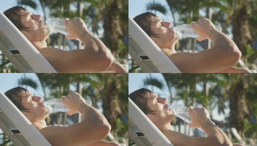 在泳池边晒太阳的帅哥从瓶子里喝水，慢动作。1920 x1080高清在线视频素材下载