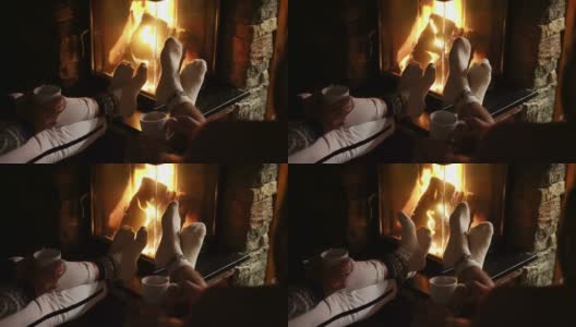 年轻夫妇在壁炉旁用圣诞装饰的袜子暖脚，喝着茶。温馨圣诞之家概念4K镜头高清在线视频素材下载