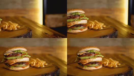 一个大的双层汉堡放在一块木板上，旁边是炸薯条。专业烹饪的快餐。高清在线视频素材下载